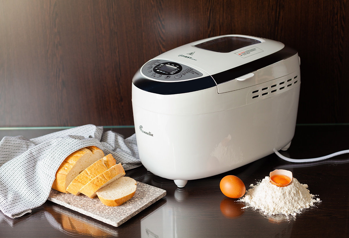 Δείχνει τον αρτοπαρασκευαστή σε πάγκο κουζίνας με δίπλα του τα υλικά αβγα, αλεύρι κ.α